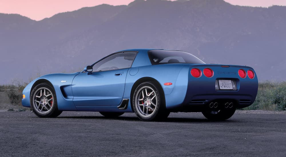 A blue 2002 Chevy Corvette Z06 is shown from a rear angle with mountains in the distance.