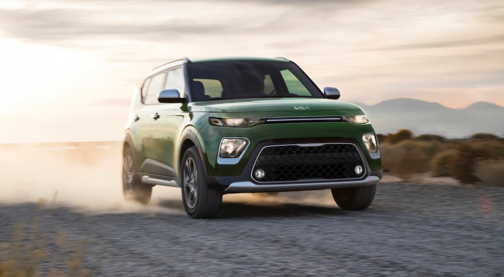 A green 2022 Kia Soul is shown driving on a dirt road.