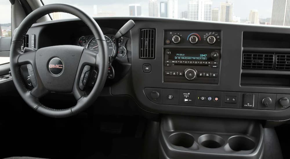 The grey interior of a 2021 GMC Savana shows the steering wheel and radio. 