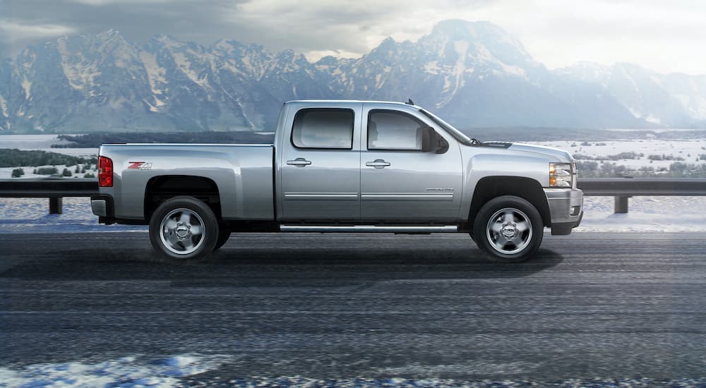 A silver 2007 Chevy Silverado 1500 is shown from the side driving in front of a mountain range.