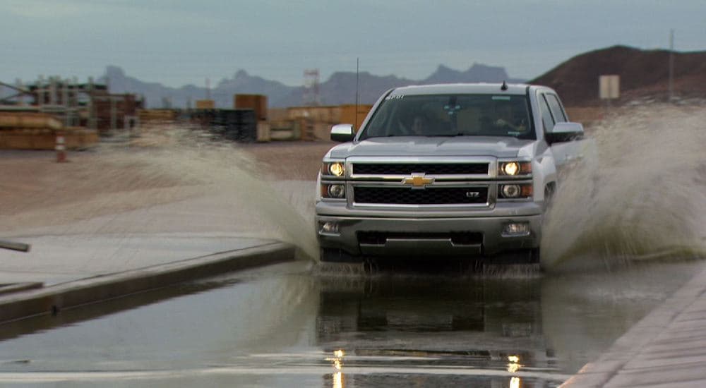 A silver 2014 Chevy Silverado 1500 is shown from the front driving through water during a durability test.