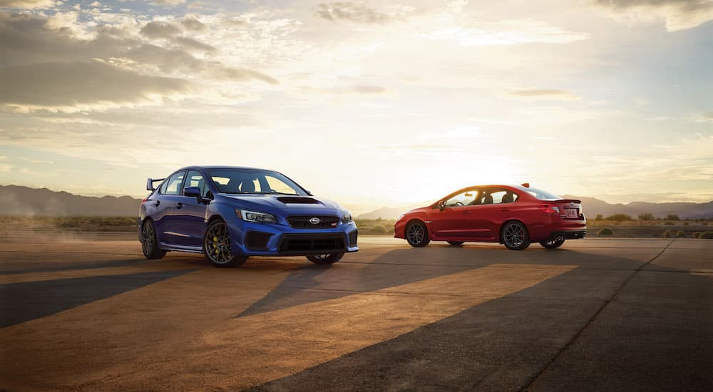 A blue 2018 Subaru WRX STI and a red 2018 Subaru WRX are shown facing opposite directions at an angle.