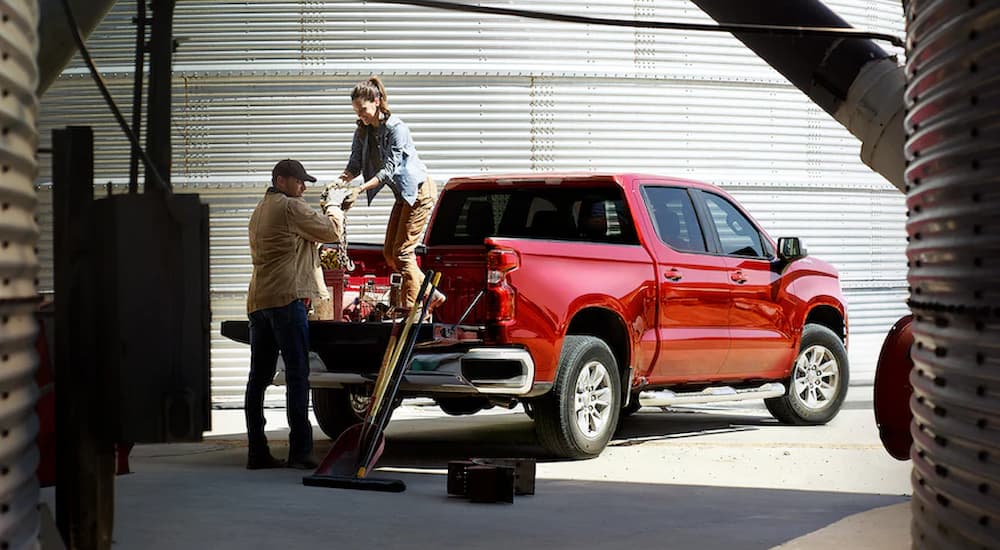 Two people are shown loading supplies into the bed of a red 2022 Chevy Silverado 1500 Limited.