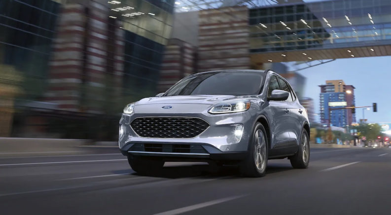 A silver 2022 Ford Escape Titanium Hybrid is show driving down a city street.