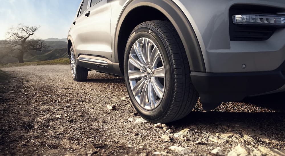 A close up shows the tire and side of a silver 2022 Ford Explorer driving on a rocky path.