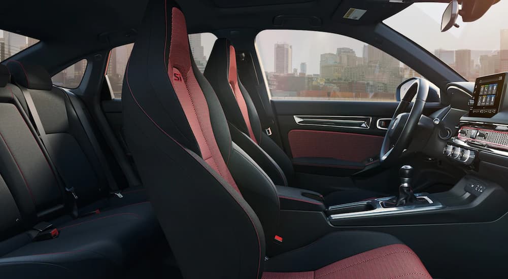 The red and black interior of a 2022 Honda Civic Si shows two rows of seating and the steering wheel.