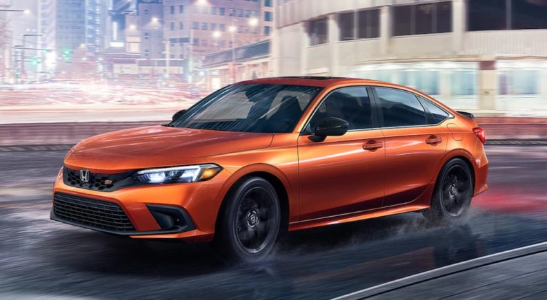 An orange 2022 Honda Civic Si is shown from the side driving through a city.