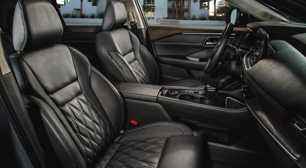 The black interior of a 2022 Nissan Rogue shows the front row seating and steering wheel.
