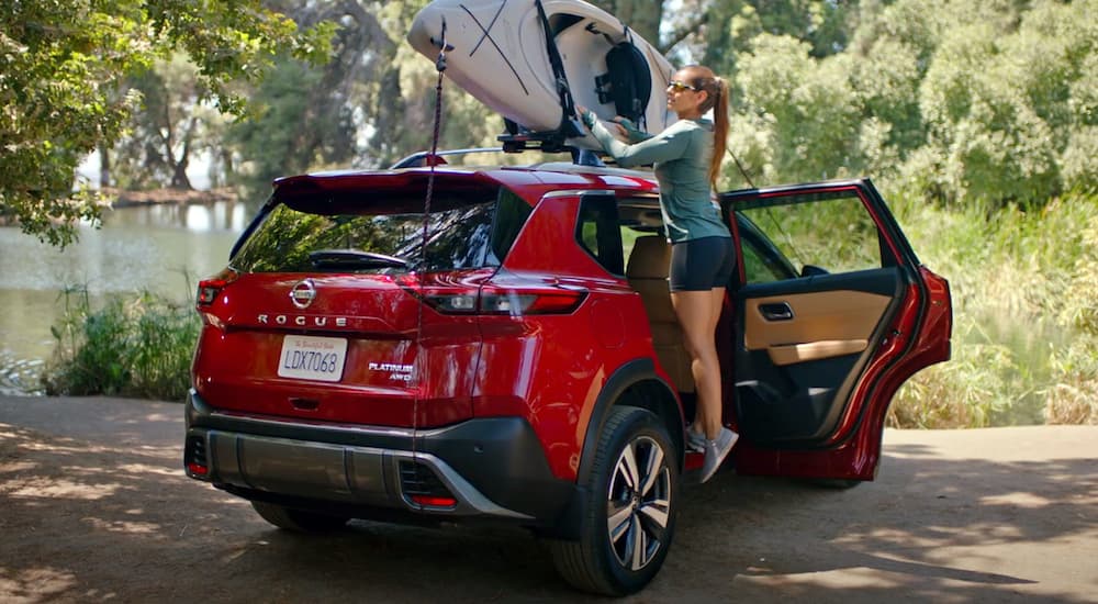 A red 2022 Nissan Rogue is shown parked as a person secures a kayak to the roof.