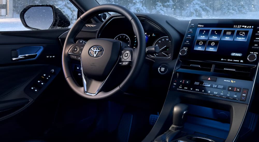 The black interior of a 2022 Toyota Avalon Limited shows the steering wheel and infotainment screen.