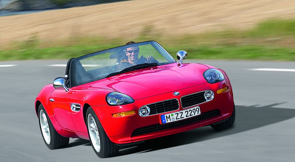 A red 2000 BMW Z8 is shown driving down an empty road after leaving a BMW dealer.