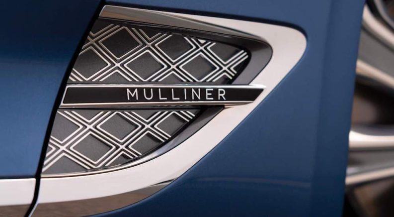 A Mulliner badge is shown on a blue Bentley up close.