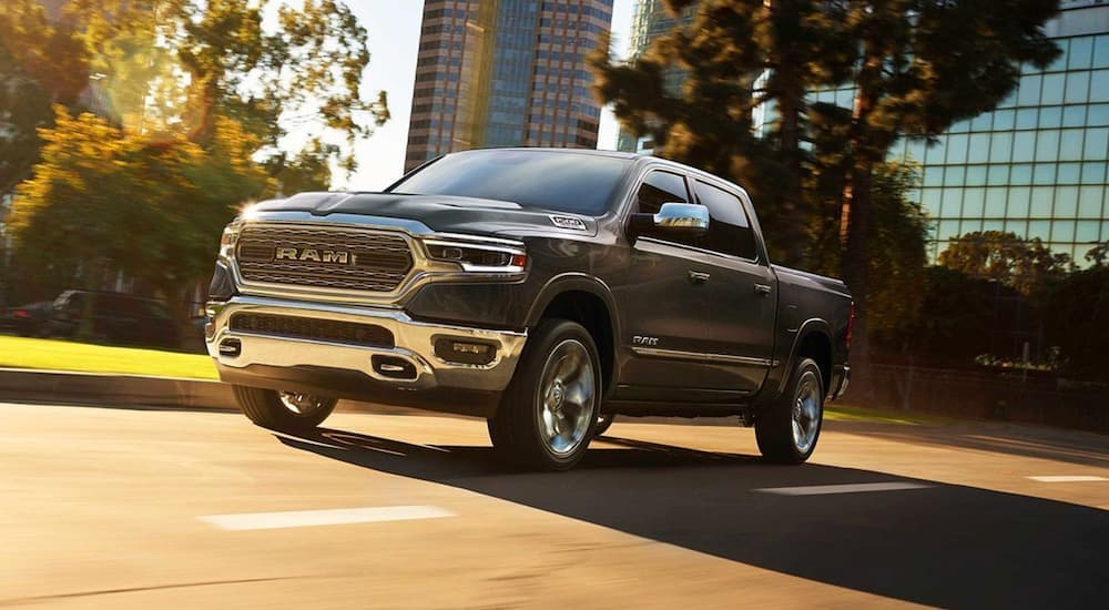 A grey 2019 Ram 1500 is shown from the front driving on an open road through a city.
