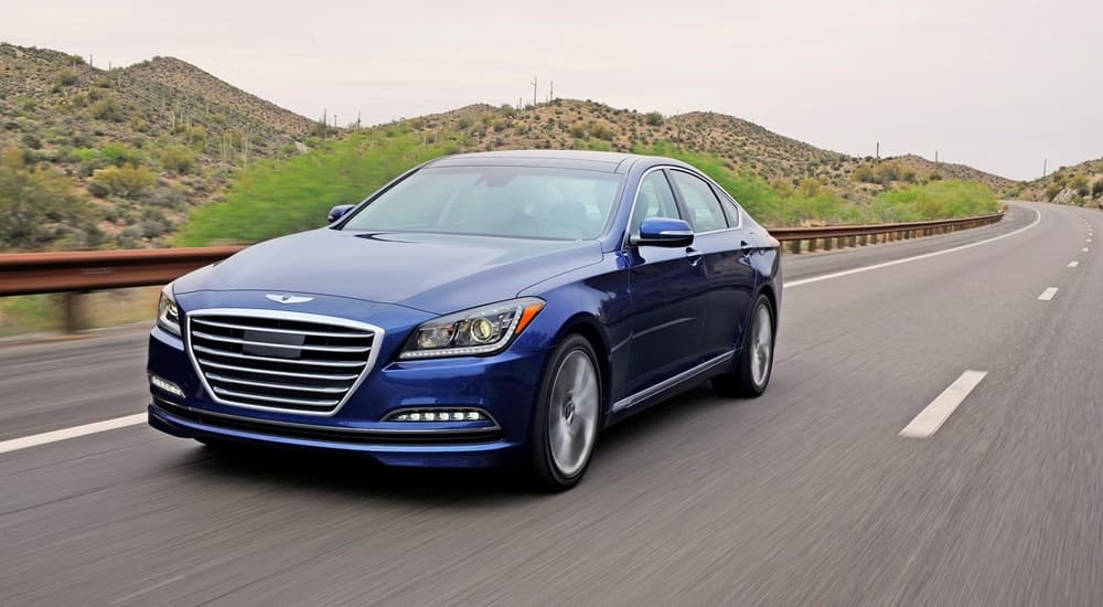 A blue 2016 Genesis is shown driving on an open road after visiting Certified Pre-Owned vehicle dealers.