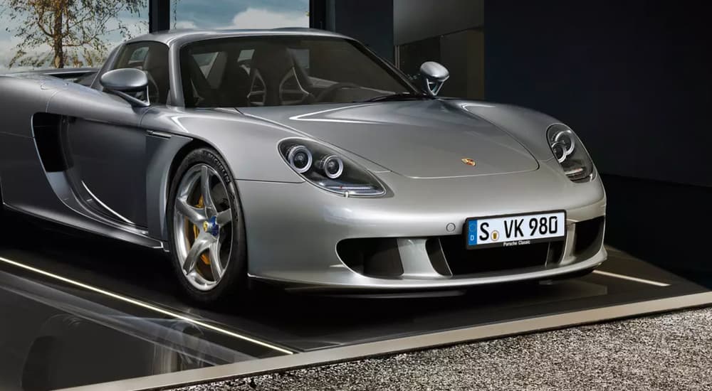 A silver 2007 Porsche Carrera GT is shown parked in a garage.