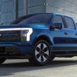 A blue 2022 Ford F-150 Lightning is shown parked in front of a Ford dealership.