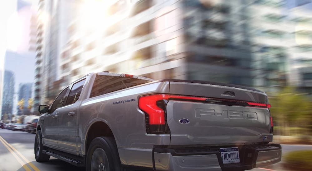 A silver 2022 Ford F-150 Lighting Lariat is shown from a rear angle driving through a city.