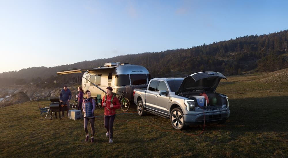 A silver 2022 Ford F-150 Lightning Platinum is shown at a campsite hitched to a silver camper.
