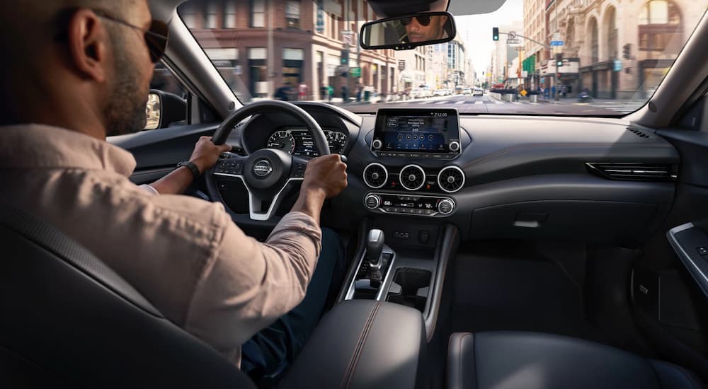 A man is shown driving and looking at the infotainment screen in a 2022 Nissan Sentra.