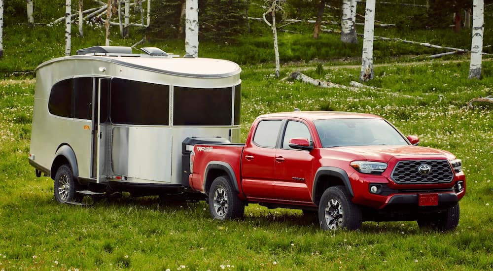 A red 2022 Toyota Tacoma TRD Off-Road is shown towing a silver camper in a grassy field.