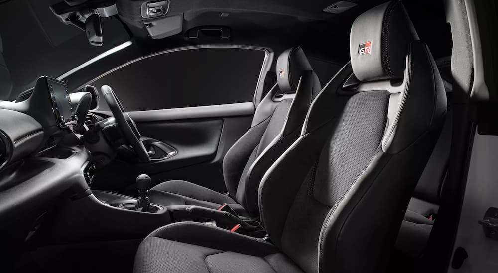 The black and red accented interior of a 2021 Toyota Yaris GR Hot Hatch shows the front seats and steering wheel.