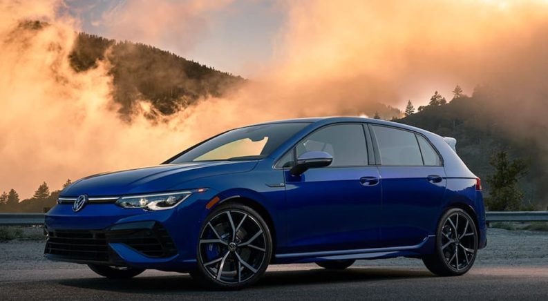 A blue 2022 Volkswagen Golf R is shown from the side parked in front of a mountain.