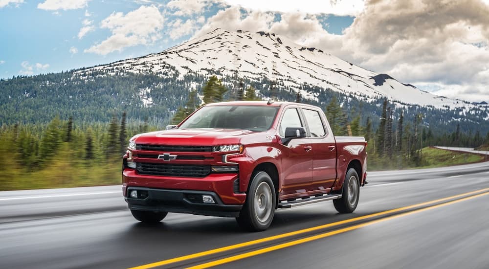A red 2022 Chevy Silverado 1500 is shown driving on a road with a mountain view.