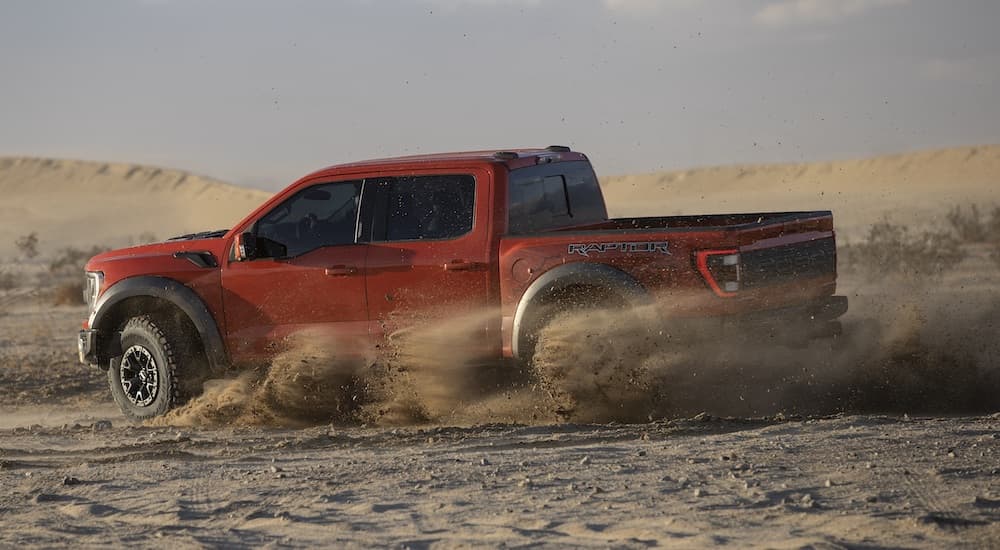A red 2021 Ford F-150 Raptor is shown from the side while it is drifting through the dirt.