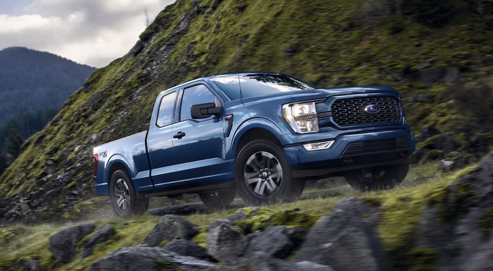 A blue 2022 Ford F-150 is shown from the side driving on the side of a mountain.