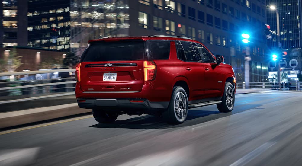 A red 2022 Chevy Tahoe is shown from the rear driving through a city at night.
