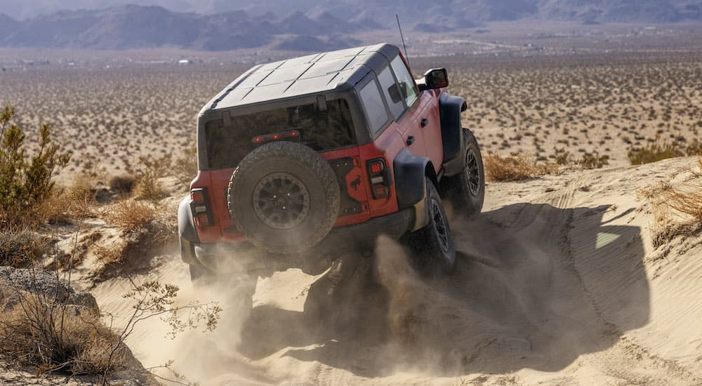A red 2022 Ford Bronco Raptor is shown from behind as it goes over rocky terrain.