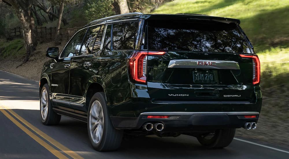 A black 2022 GMC Yukon Denali is shown from the rear driving on a shaded road.