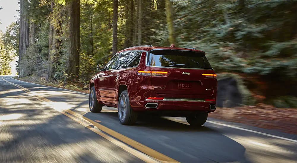 A red 2022 Jeep Grand Cherokee L is shown from behind driving on a wooded road.