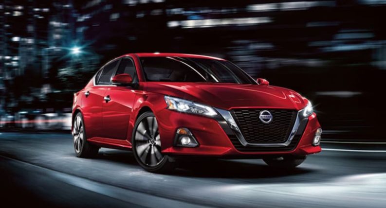 A red 2022 Nissan Altima is shown driving through a city at night.