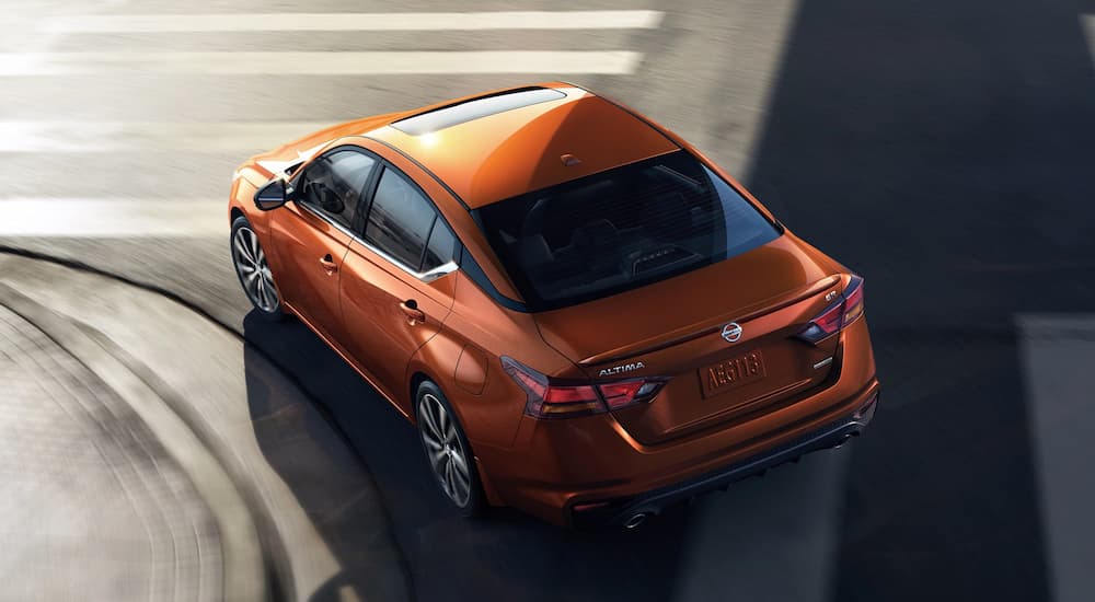 An orange 2022 Nissan Altima is shown from the rear while driving on a city street.