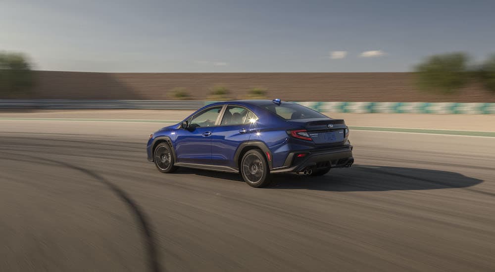 A blue 2022 Subaru WRX is shown from the rear driving on a race track.