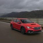 A red 2022 Subaru WRX is shown driving past a river.