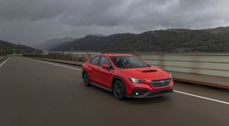 A red 2022 Subaru WRX is shown driving past a river.