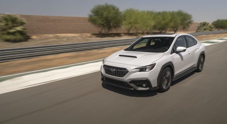 A white 2022 Subaru WRX is shown driving on an empty road.
