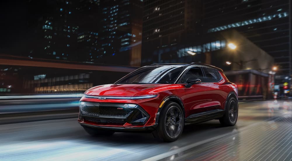 A red 2024 Chevrolet Equinox EV RS is shown from a front angle driving through a city at night.