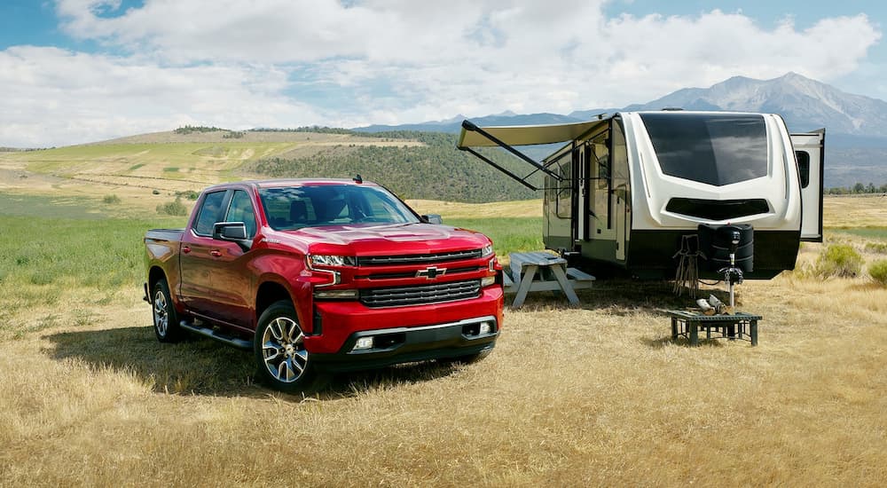 A red 2022 Chevy Silverado 1500 LTD RST is shown parked next to a camper trailer.