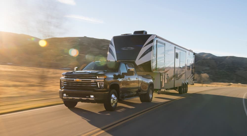 A black 2022 Chevy Silverado 3500HD is shown towing a fifth-wheel camper trailer.
