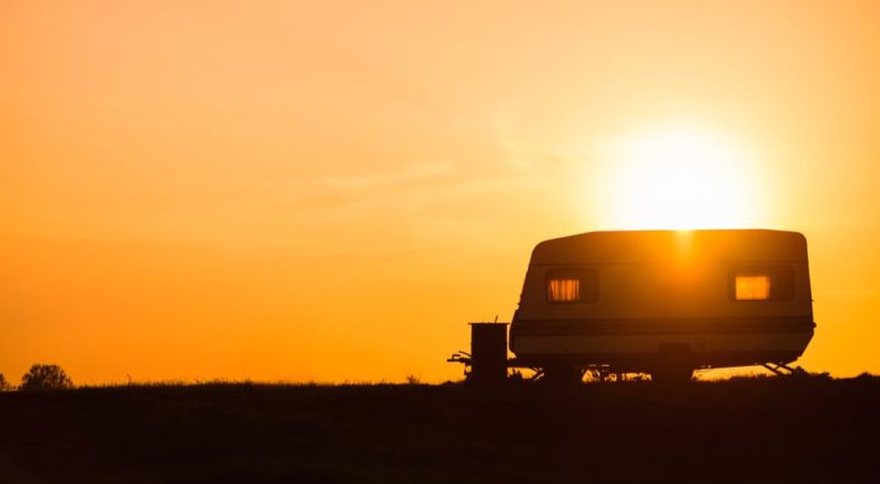 A camping trailer is shown parked on top of a hill during a sunset.