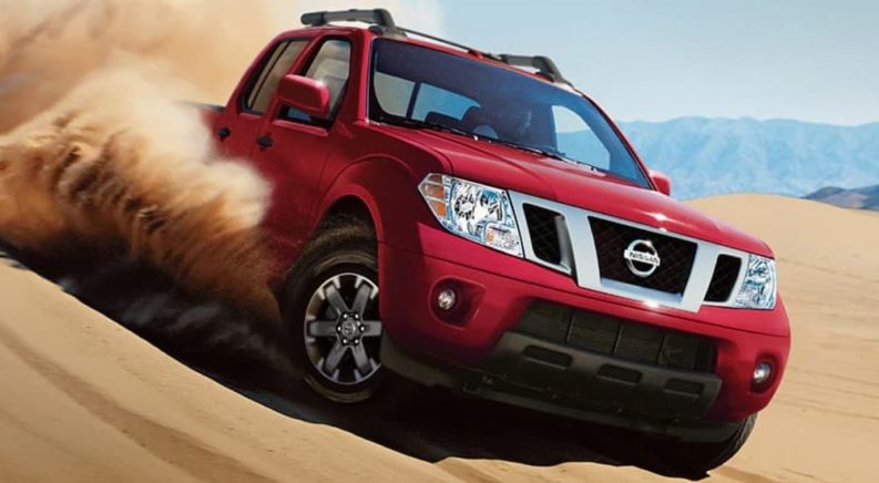 A red 2021 Nissan Frontier is shown off-roading in a desert after leaving a Certified Pre-Owned Nissan Frontier dealership.