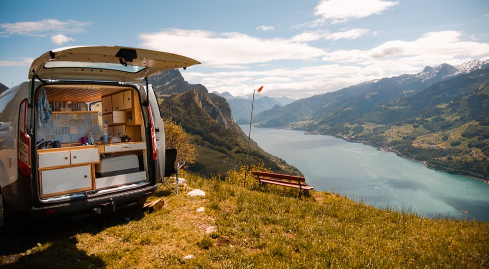A converted commercial van is shown with parked on top of mountain with a lake view.