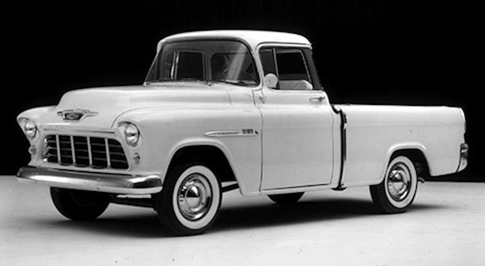 A white 1955 Chevy Cameo Carrier is shown from the side at a Ford dealership.