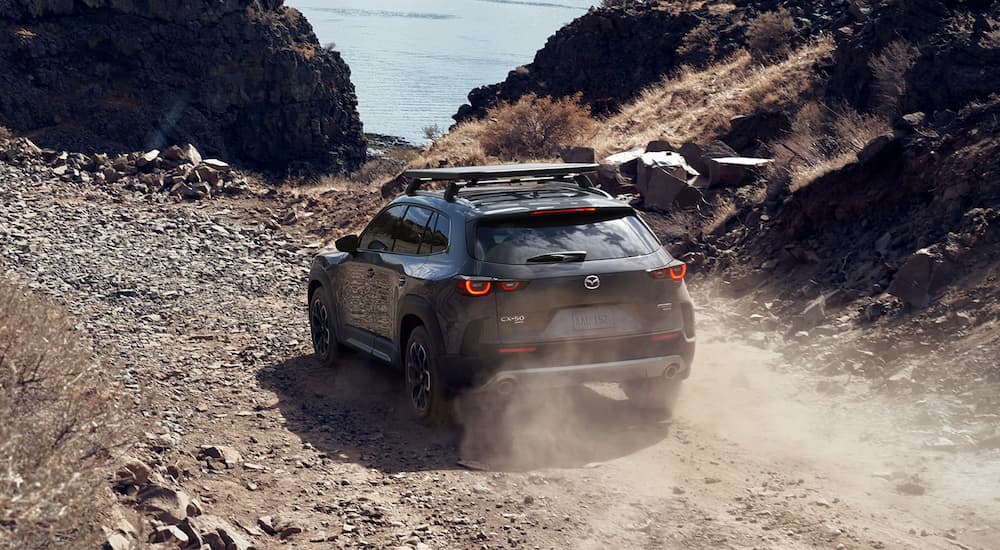 A dark grey 2023 Mazda CX-50 is shown from the rear driving on a rocky path.