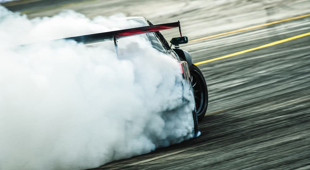 A race car is shown from the rear with tire smoke on a racetrack.