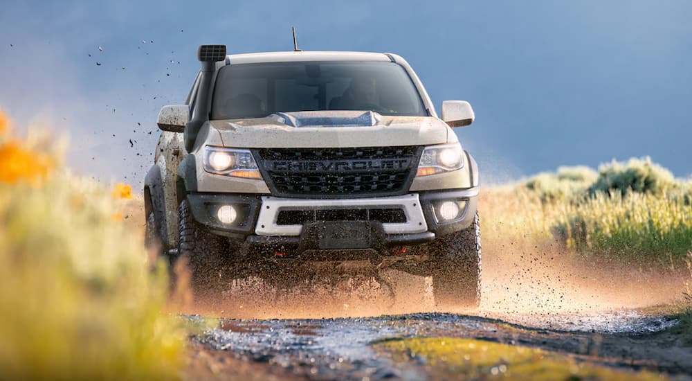 A tan 2022 Chevy Colorado ZR2 is shown from the front off-roading on a muddy road.