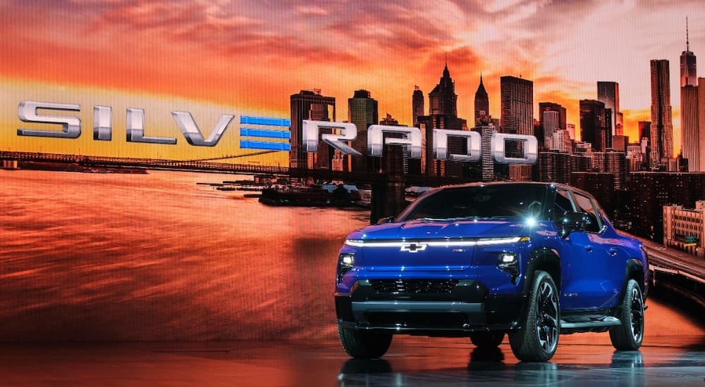 A blue 2024 Chevy Silverado EV is shown from the front at an angle on a stage.